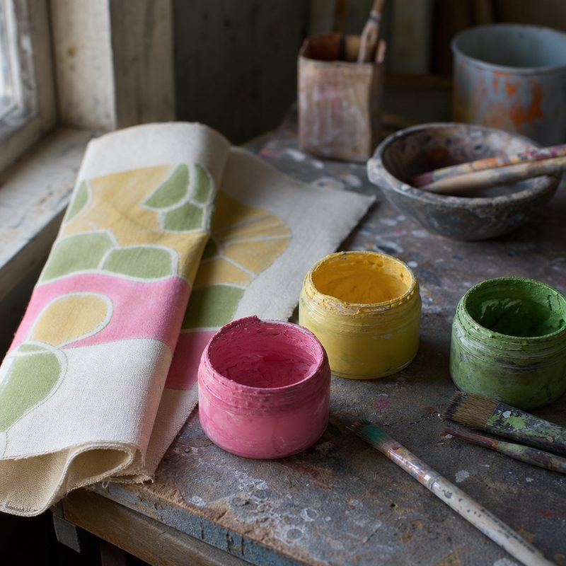 Jars of fluorescent pigment reading as pastel colours on a painter's table in workshop daylight